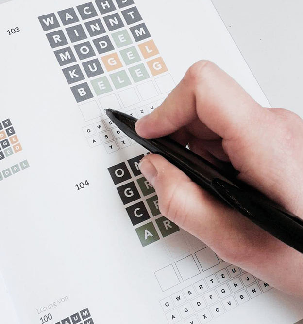 Hand mit Kugelschreiber füllt Wordle Rätsel aus